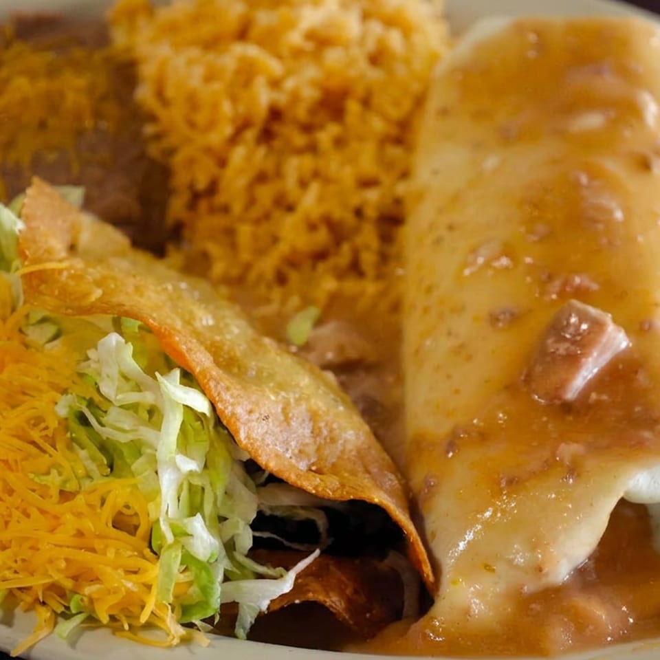 Plate of Mexican food featuring a burrito with sauce, crispy taco, refried beans, rice, lettuce, and shredded cheese.