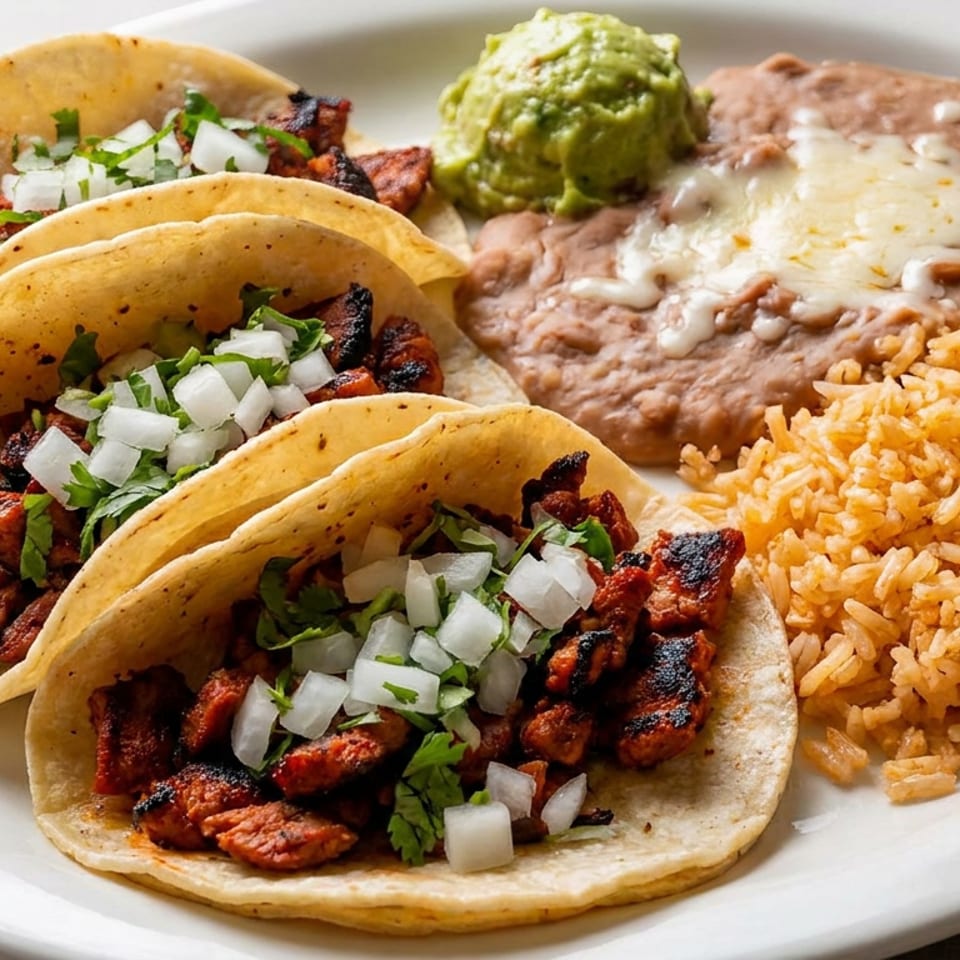 Three grilled meat tacos with onion and cilantro, served with guacamole, refried beans topped with cheese, and Mexican rice.