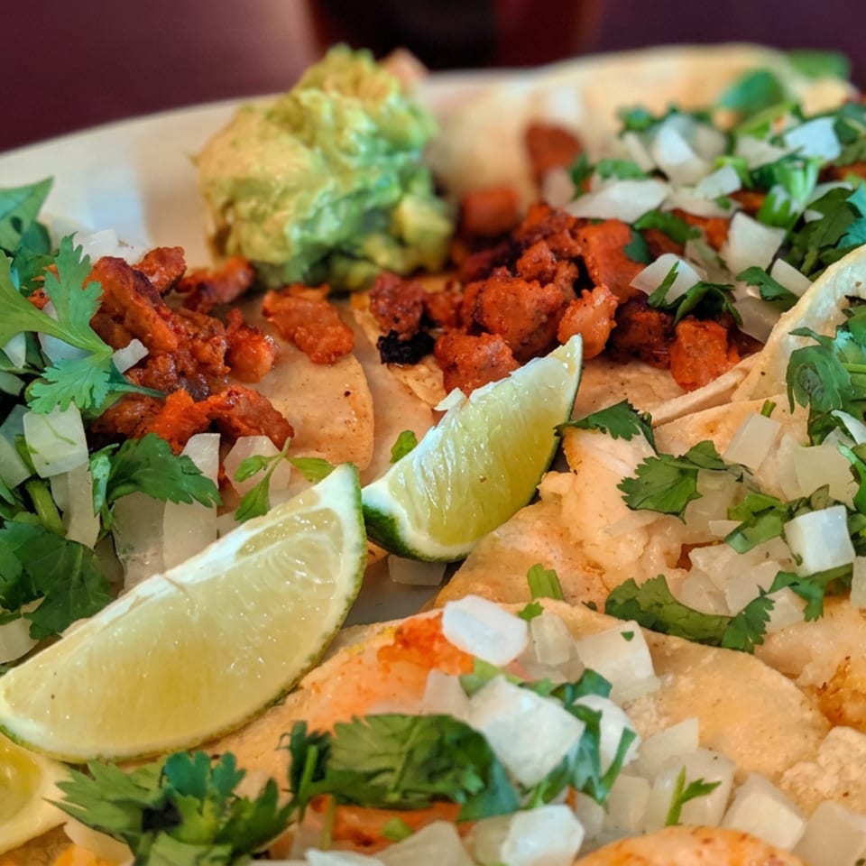 Assorted Mexican tacos topped with cilantro and onions, served with lime wedges and guacamole on a platter.